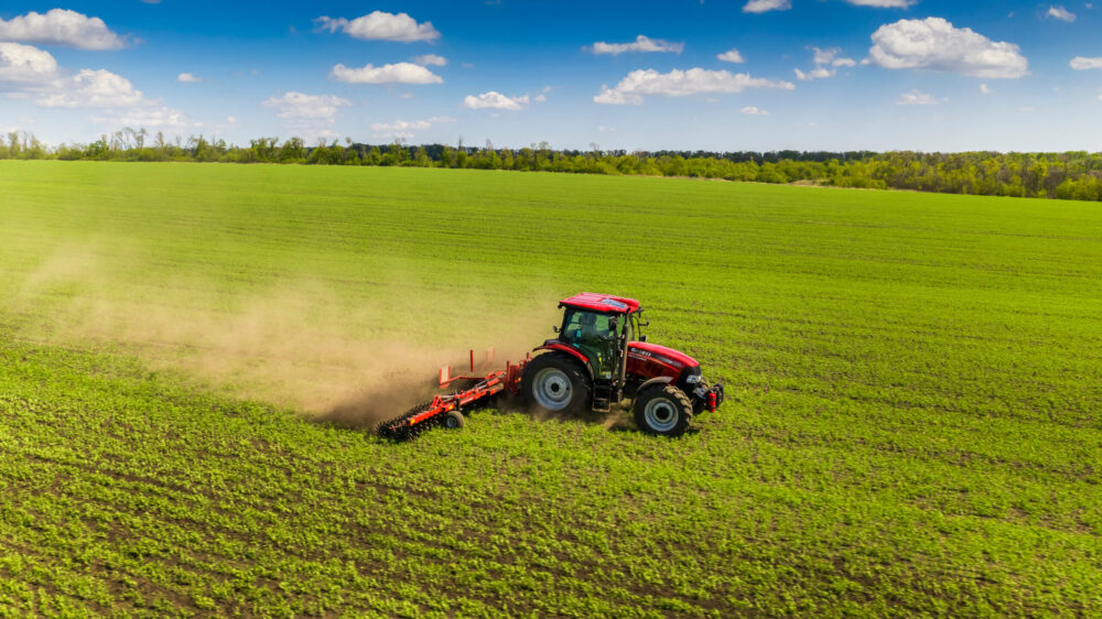 Image of a red tractor working a field of green crops utilizing agricultural hydraulic oils