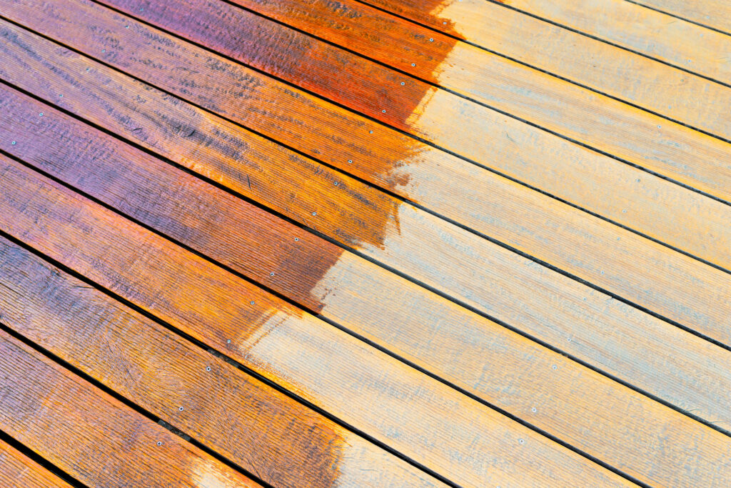Close-up of a wooden deck showing the process of restoration with half a sealed surface contrasting weathered wood during a home improvement project