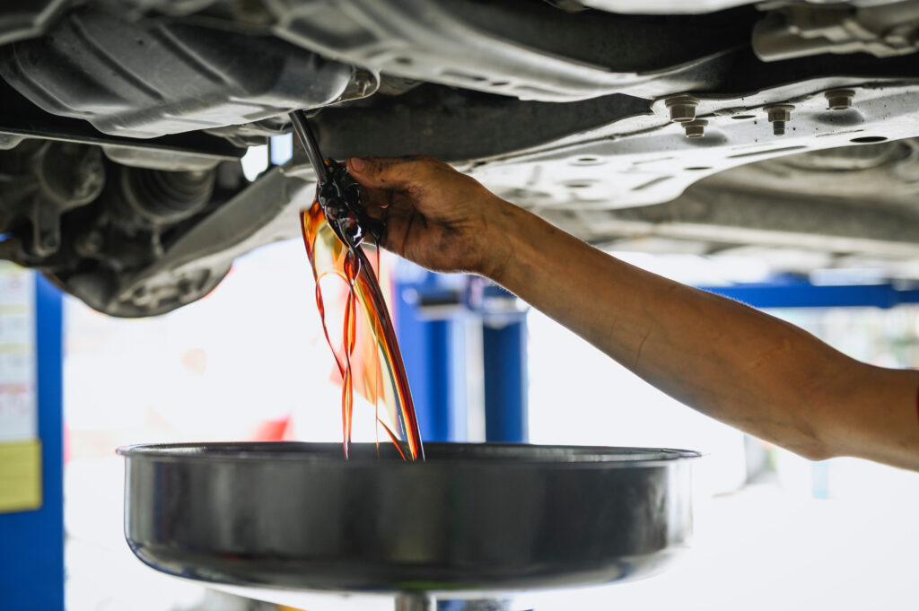 Auto mechanic draining dirty engine oil during an oil change.