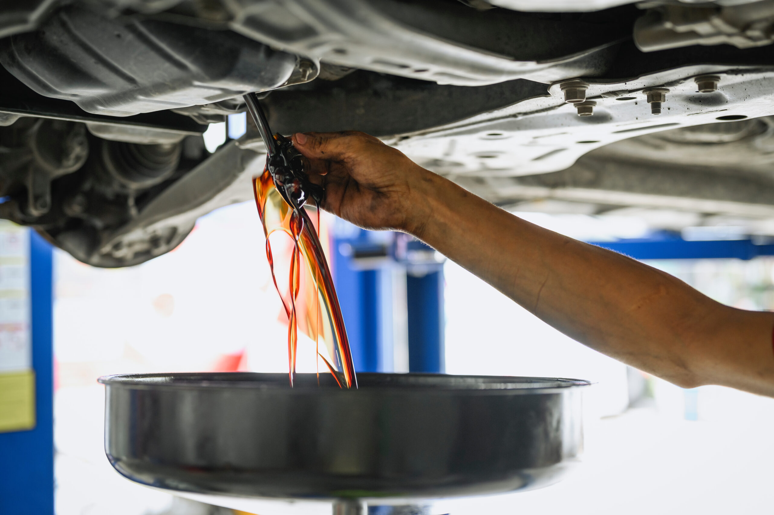 Auto mechanic draining dirty engine oil during an oil change.