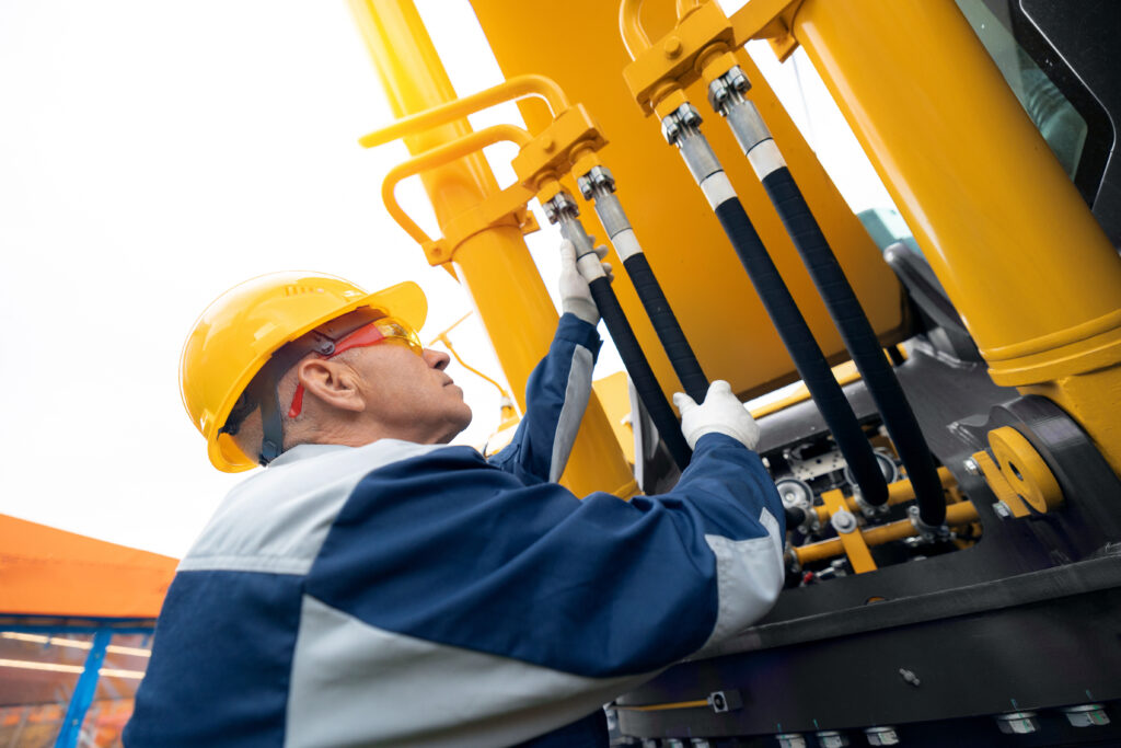 Machinery tractor mechanic checks hydraulic hose system equipment on excavator.